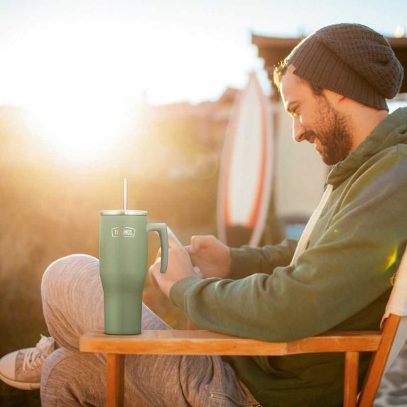 En mann sitter ute i str�lende solskinn, ved bordet hvor han sitter st�r det en gr�nn Thermos-termoskopp. 